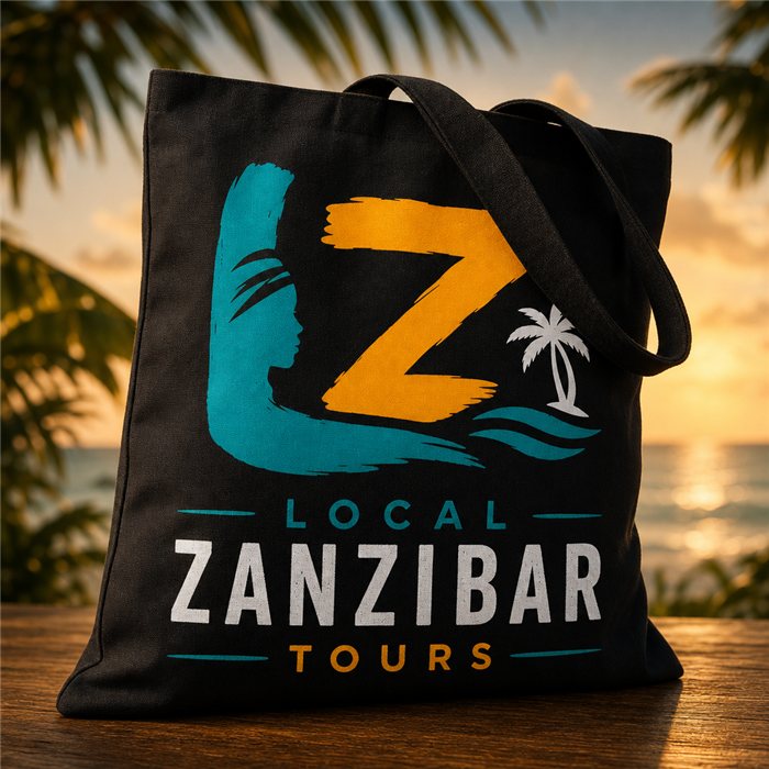 Zwarte katoenen tas met het Local Zanzibar Tours-logo: turquoise en gele letters met palmboom, op een tafel bij zonsondergang